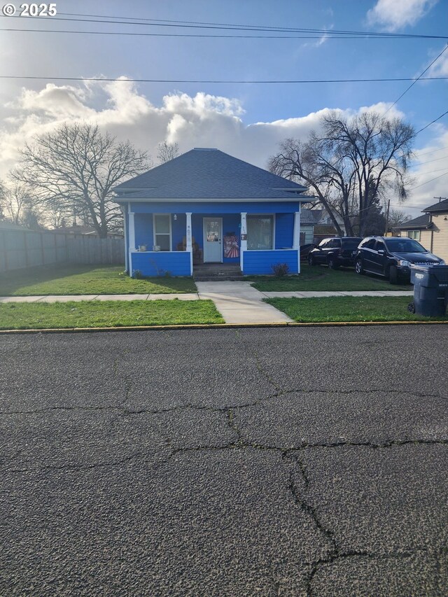 view of front of property with a front lawn, a shingled roof, and fence