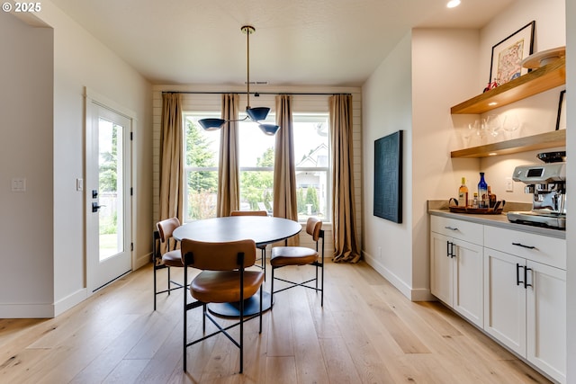 dining area featuring a bar, light wood finished floors, healthy amount of natural light, and baseboards