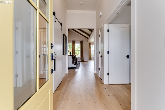 hall with light wood-type flooring, a barn door, ornamental molding, and baseboards