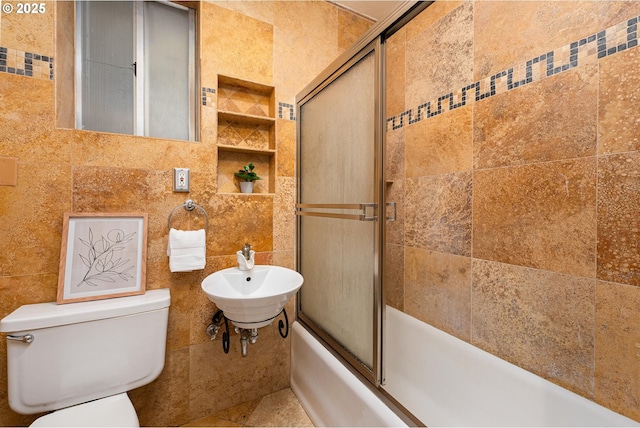 full bathroom featuring combined bath / shower with glass door, a sink, tile walls, and toilet