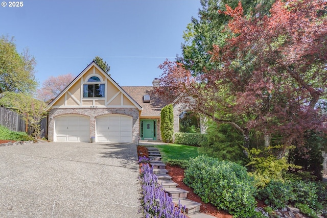 english style home featuring roof with shingles, fence, brick siding, driveway, and a chimney