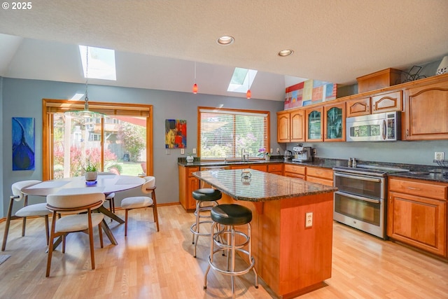 kitchen with light wood-style flooring, a center island, lofted ceiling with skylight, a sink, and appliances with stainless steel finishes