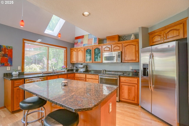 kitchen featuring lofted ceiling with skylight, a sink, stainless steel appliances, brown cabinetry, and light wood-style floors