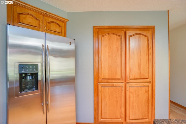 kitchen with brown cabinetry, baseboards, and stainless steel refrigerator with ice dispenser