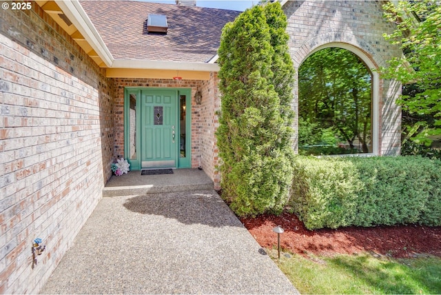 doorway to property featuring a shingled roof and brick siding