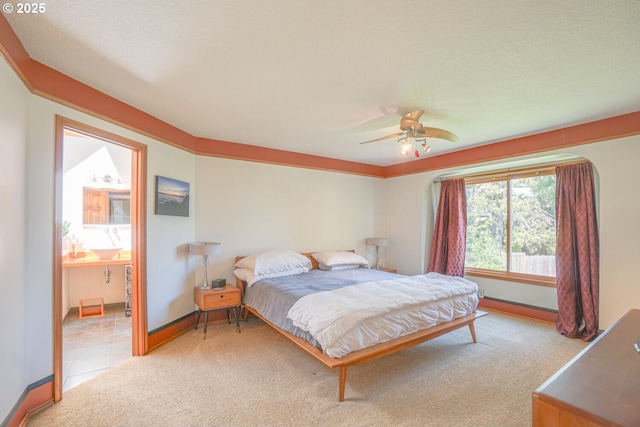 bedroom with ensuite bath, light carpet, baseboards, and a ceiling fan