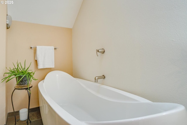 bathroom featuring tile patterned floors, a freestanding bath, and vaulted ceiling