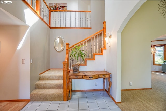stairs with arched walkways, baseboards, carpet flooring, and a towering ceiling
