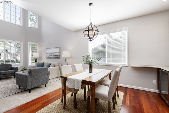 dining room with baseboards, a towering ceiling, wood finished floors, and a notable chandelier