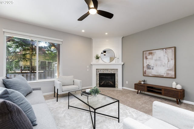 living room with a high end fireplace, a ceiling fan, and light colored carpet