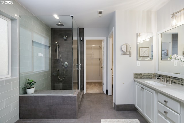 bathroom featuring a walk in closet, decorative backsplash, visible vents, a shower stall, and vanity