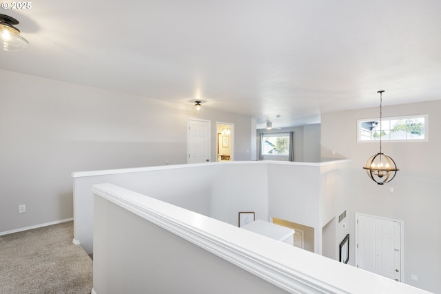hallway featuring visible vents, baseboards, carpet flooring, a notable chandelier, and an upstairs landing