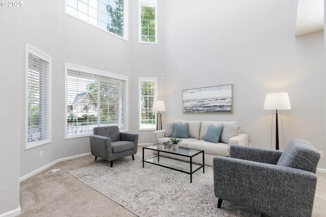 carpeted living area with plenty of natural light, baseboards, a high ceiling, and visible vents