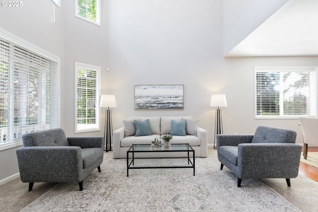 living area with baseboards, a wealth of natural light, carpet, and a towering ceiling