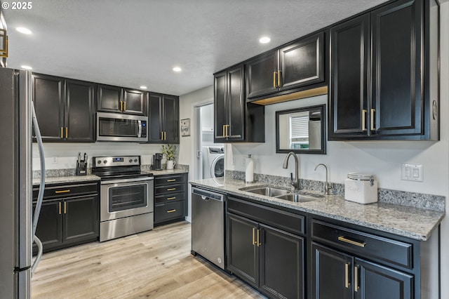 kitchen with appliances with stainless steel finishes, light wood-type flooring, washer / dryer, light stone counters, and sink