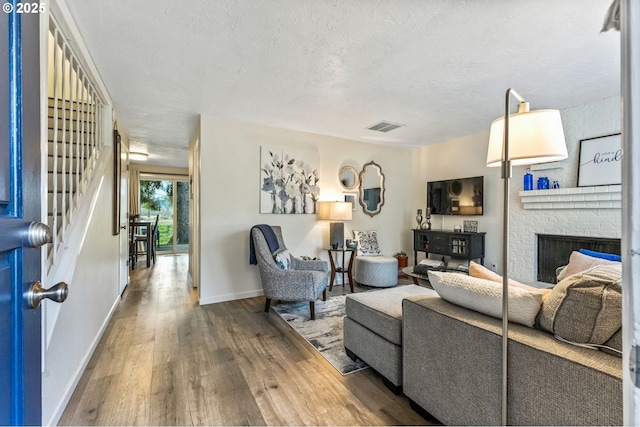 living room featuring a brick fireplace, a textured ceiling, and hardwood / wood-style floors