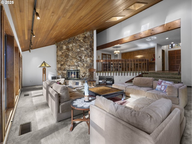 carpeted living room with rail lighting, a stone fireplace, a chandelier, wooden ceiling, and a towering ceiling