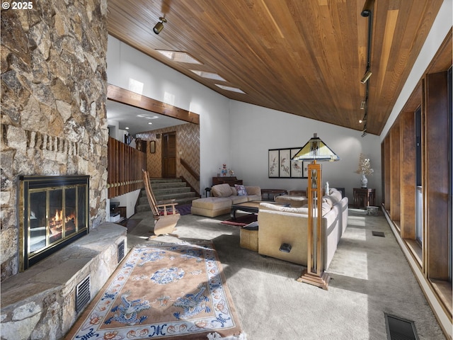 living room featuring rail lighting, a stone fireplace, carpet flooring, and wood ceiling