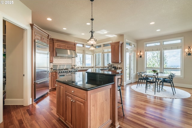 2640 NW Birkendene St, Portland, OR 97229 - kitchen featuring high end appliances, under cabinet range hood, wood finished floors, a breakfast bar, and baseboards