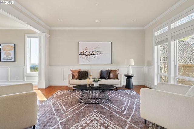 living room with wood finished floors, a wainscoted wall, ornamental molding, and decorative columns