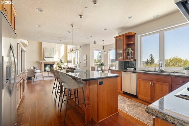 kitchen featuring a sink, brown cabinetry, stainless steel appliances, a kitchen bar, and dark wood-type flooring