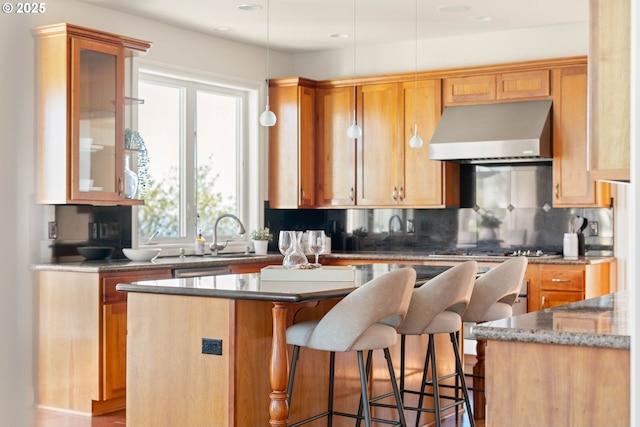kitchen featuring a kitchen breakfast bar, under cabinet range hood, backsplash, a center island, and dark stone counters