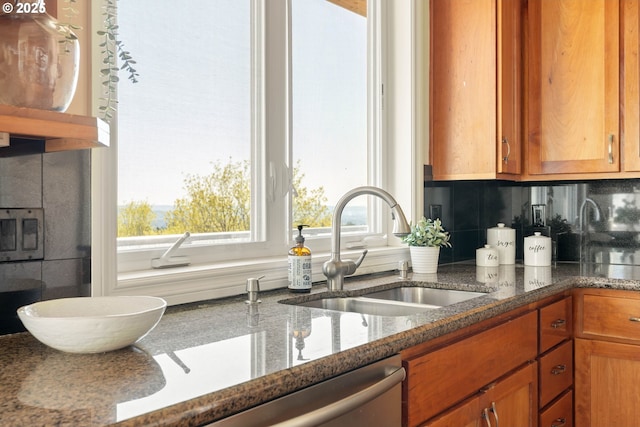 kitchen featuring brown cabinets, backsplash, dark stone counters, and a sink