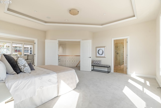 bedroom featuring a raised ceiling, light colored carpet, and ensuite bathroom