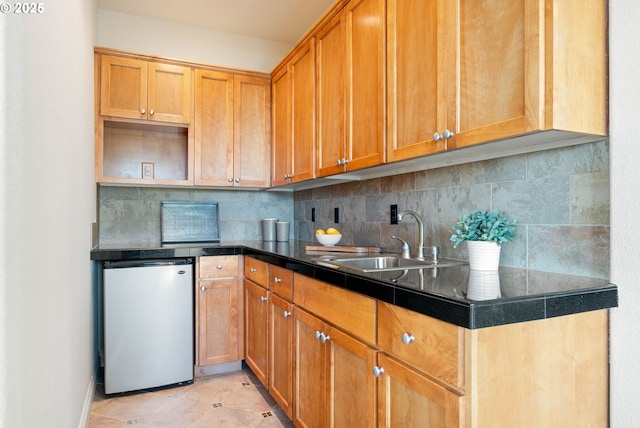 kitchen featuring backsplash, dark countertops, fridge, and a sink