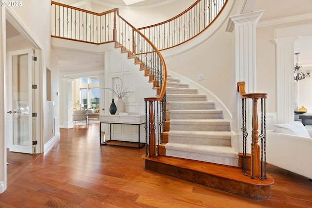 stairway featuring decorative columns, wood finished floors, a high ceiling, and ornamental molding