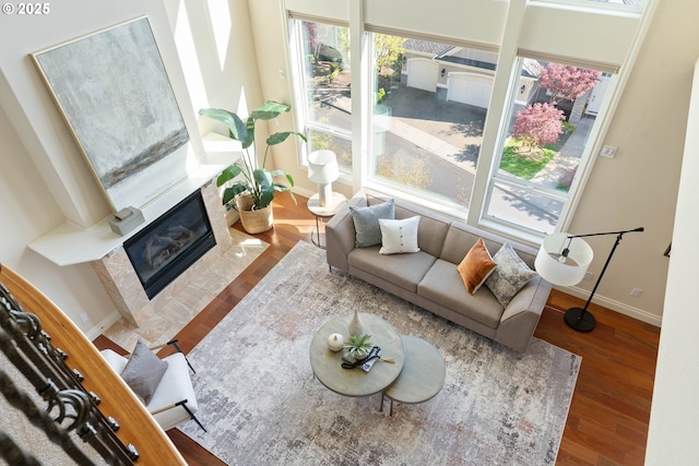 living room with a tiled fireplace, baseboards, and wood finished floors