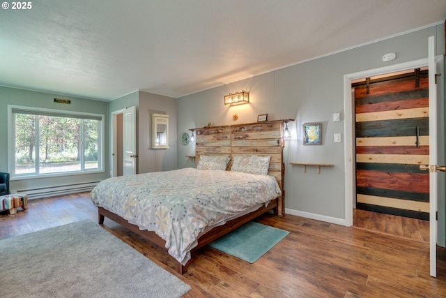 bedroom featuring a barn door, wood finished floors, baseboards, and baseboard heating