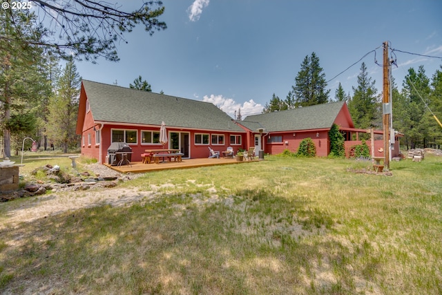 rear view of house with a lawn, a shingled roof, and a deck