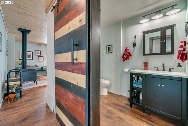 bathroom with vanity, a wood stove, toilet, and wood finished floors