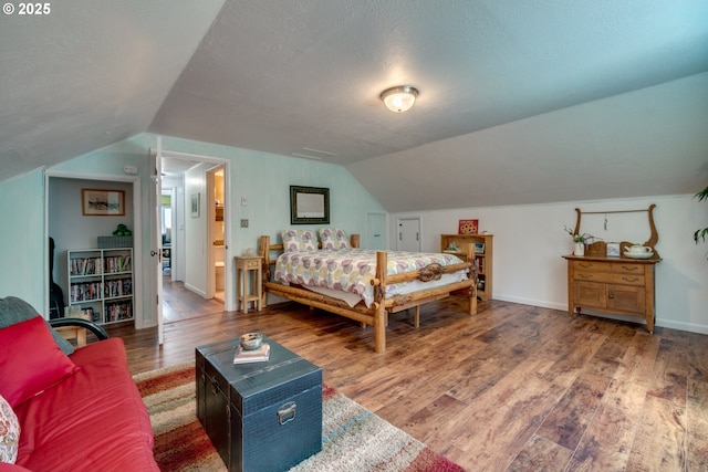 bedroom with a textured ceiling, wood finished floors, and vaulted ceiling