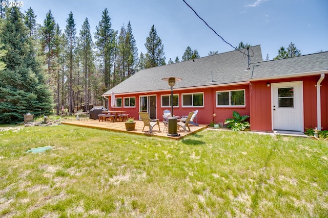 back of property with a deck, a lawn, an outdoor fire pit, and roof with shingles