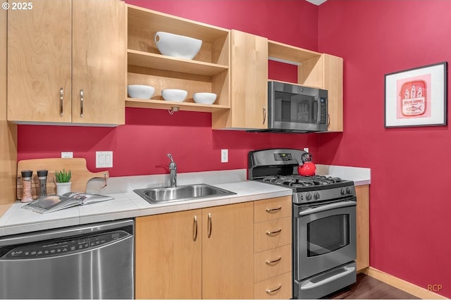 kitchen featuring a sink, baseboards, appliances with stainless steel finishes, and light brown cabinetry