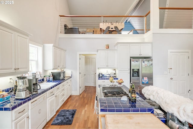 895 Pine Forest Dr, Eugene, OR 97405 - kitchen featuring a high ceiling, tile countertops, stainless steel appliances, light wood-style flooring, and white cabinets