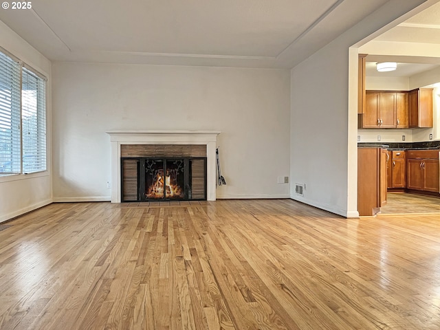 unfurnished living room with visible vents, light wood-style flooring, baseboards, and a lit fireplace