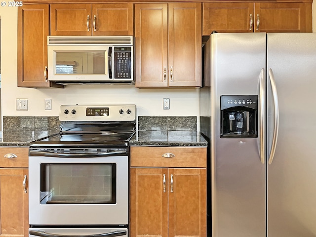 kitchen with dark stone counters, appliances with stainless steel finishes, and brown cabinetry