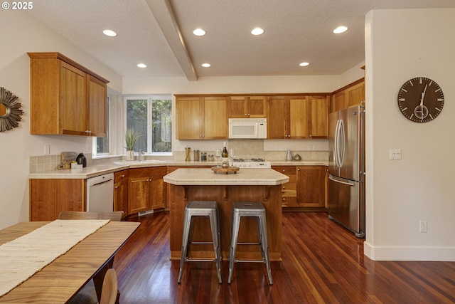 kitchen with a sink, brown cabinetry, a kitchen island, white appliances, and a textured ceiling
