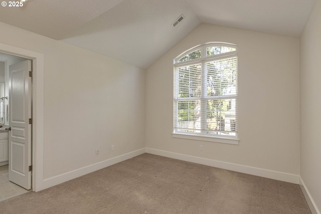 spare room featuring visible vents, baseboards, vaulted ceiling, and light carpet