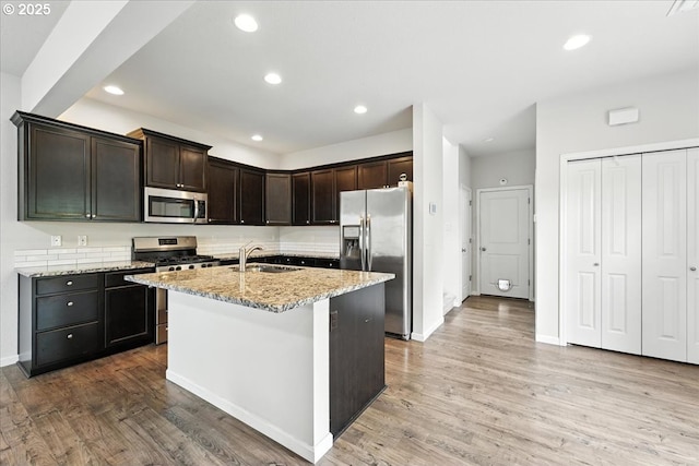 2103 SE 18th Aly, Gresham, OR 97080 - kitchen with stainless steel appliances, light stone counters, wood finished floors, dark brown cabinetry, and a kitchen island with sink