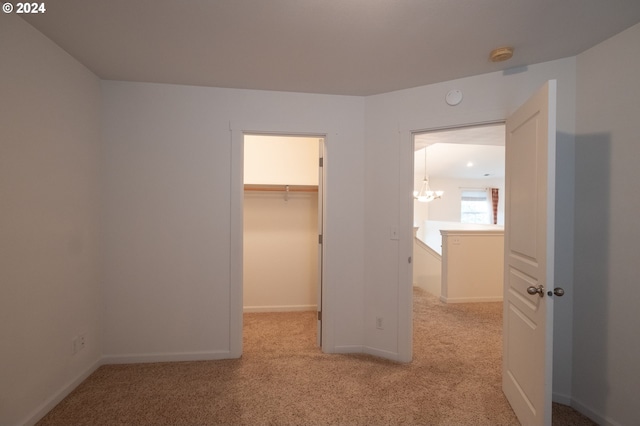 unfurnished bedroom with a walk in closet, a closet, light colored carpet, and a chandelier