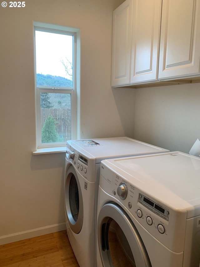 laundry area with cabinets, a wealth of natural light, independent washer and dryer, and light hardwood / wood-style flooring