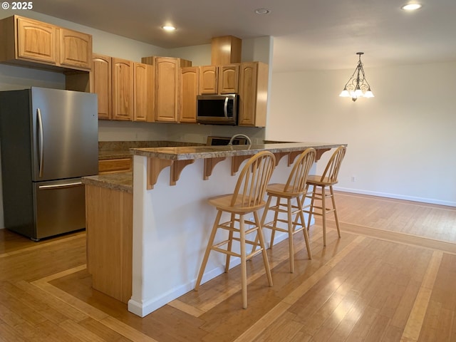 kitchen with stainless steel appliances, pendant lighting, a breakfast bar, and a notable chandelier