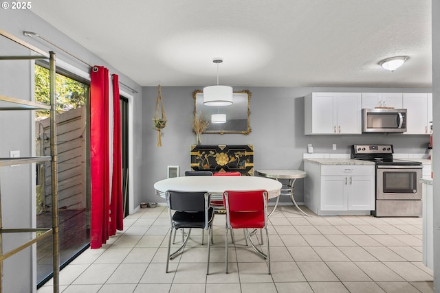 kitchen with hanging light fixtures, stainless steel appliances, white cabinets, and light tile patterned flooring