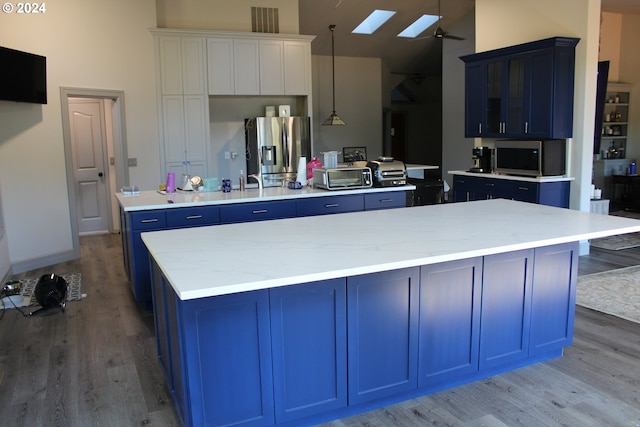 kitchen featuring light wood-style flooring, appliances with stainless steel finishes, a skylight, a large island, and blue cabinets