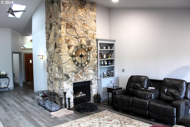 living area with wood finished floors, a high ceiling, a stone fireplace, and a skylight