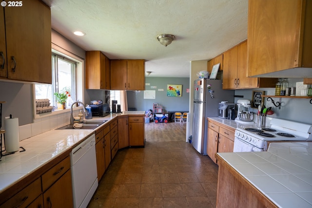 kitchen featuring white appliances, tile counters, a sink, and brown cabinetry